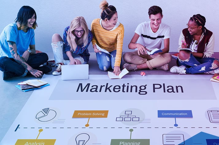 Gruppe von diversen jungen Erwachsenen sitzt auf dem Boden und arbeitet an einem Marketingplan mit Diagrammen und Büchern, was Teamarbeit im digitalen Marketing darstellt.